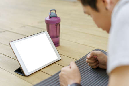 Happy Asian young man doing a plank exercise and watching on a tablet, tablet isolated screen. Man...