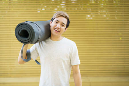 Active Asian sportsman preparing - unrolling an exercise or Yoga mat, healthy and fit body of Asian sport man preparing a workout yoga mat for body weight and cardio exercise.の写真素材