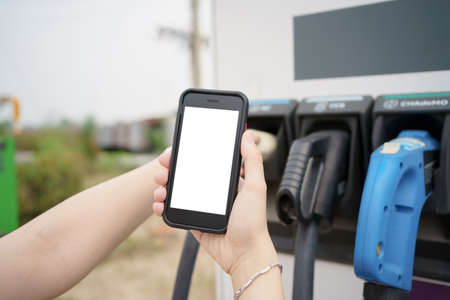 Empty screen of mockup smartphone. Asian young woman using ev charging application on smartphone connect with the charging station, BEV or electric vehicle charging stationの写真素材