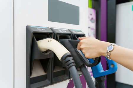 Unrecognizable Asian woman holding a DC - CCS type 2 EV charging connector at EV charging station,...