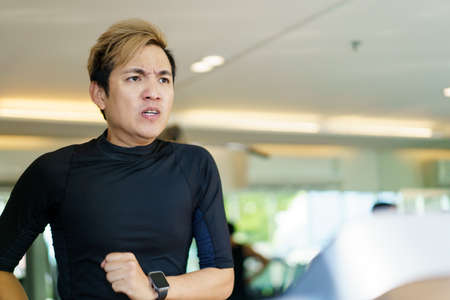 Active Asian sportsman making a cardio exercise by running on the treadmill machine in a fitness or gym, healthy sport man doing a cardio workout.の写真素材