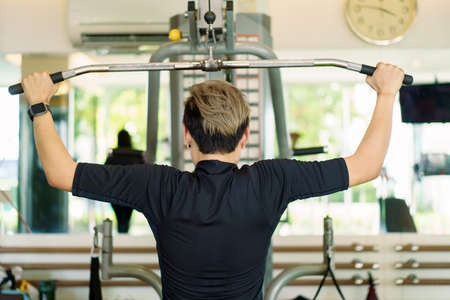 Active young Asian sportsman practice weight training in the gym by using weight pulldown machine....