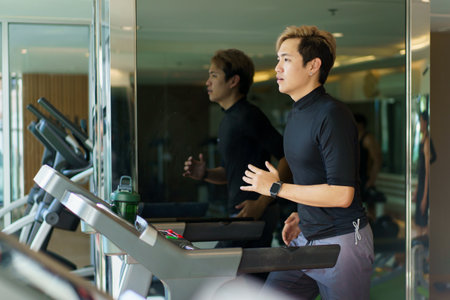 Active Asian sportsman making a cardio exercise by running on the treadmill machine in a fitness or...