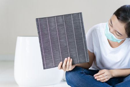 Asian woman wearing a hygiene protective face mask during changing a dirty air filter in the air purifier machine close up with copyspace. Hygienic lifestyle and prevention from illness concept.の写真素材
