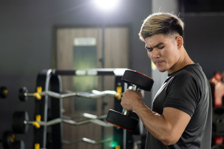 Powerful sportive man lifting up a heavy barbell in a gym, body building exercise. Body building workout in an indoor gym. Man making a muscular and bodybuilding training.の写真素材