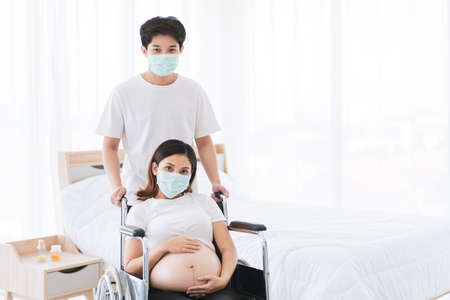 Husband take care his pregnant wife sitting on a wheelchair, husband stay beside his wife together...