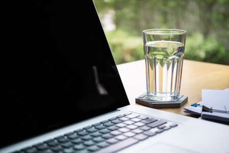 Mineral drinking water in a glass on a desk with laptop computer. Refreshment and relaxation after working concept, work life balance. Home office workplace in modern working lifestyle.の写真素材