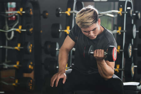 Asian young man practice weight training workout in the gym, body building exercise. Muscle building challenge concept. Strong sportsman lift up a dumbbell close up with copy space.の写真素材