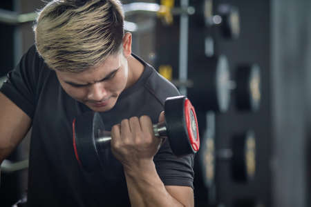 Asian young man practice weight training workout in the gym, body building exercise. Muscle building challenge concept. Strong sportsman lift up a dumbbell close up with copy space.の写真素材