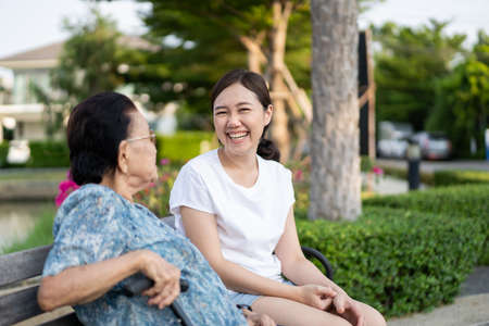 Grandma sitting beside her granddaughter in a park. Young woman taking care of elder person in a...