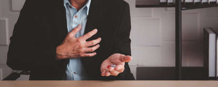 Elder Asian business man got a sickness and stressed disease in working lifestyle. Old man preparing a painkiller pills on hand close up. Office lifestyle without work life balance and unhealthy life.の写真素材