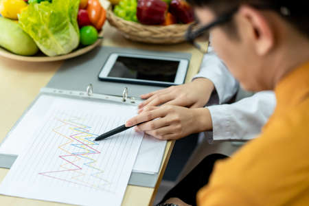 Young Asian man come to meet the nutritionist in hospital and talking about dieting and eating. Expertise nutritionist giving a eating recommendation to a man who have health problem.の写真素材