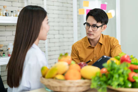 Young Asian man come to meet the nutritionist in hospital and talking about dieting and eating. Expertise nutritionist giving a eating recommendation to a man who have health problem.の写真素材
