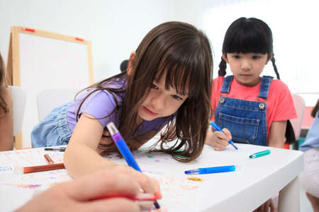 Happy caucasian and Asian young elementary school age enjoy learning and playing in their classroom with their teacher. Boys and girls studying arts and mathematics in classroom.の写真素材