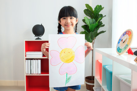 Happy little Asian girl showing her painting - drawing art on a paper to camera. Education and development in the elementary or preschool age concept. Kindergarten children portrait.の写真素材