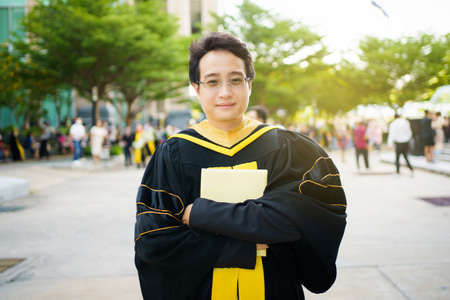 Happy Asian graduate student holding the diplomas on hand during the university graduation ceremony. Master degree student in gown suit holding a diplomas for photography.の写真素材