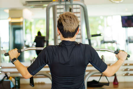 Active young Asian sportsman practice weight training in the gym by using weight pulldown machine....