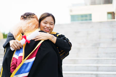Happy Asian young women in the master degree gown showing a diploma in their hand close up. Portrait of confident college students in gown in the graduation ceremony.の写真素材