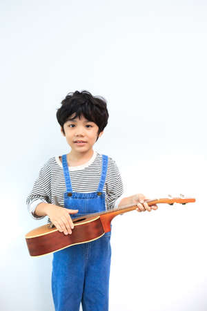Happy Asian little boy enjoy practicing an acoustic guitar and smiling to camera for photography....