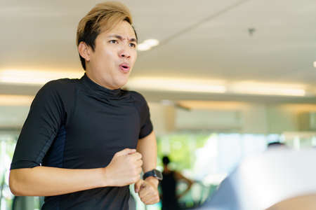 Active Asian sportsman making a cardio exercise by running on the treadmill machine in a fitness or gym, healthy sport man doing a cardio workout.の写真素材