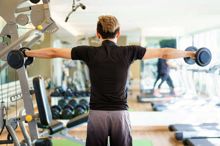 Active Asian sportsman doing a weight exercise in a gym - fitness by lifting up a dumbbell, man...