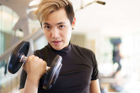 Active Asian sportsman doing a weight exercise in a gym - fitness by lifting up a dumbbell, man...