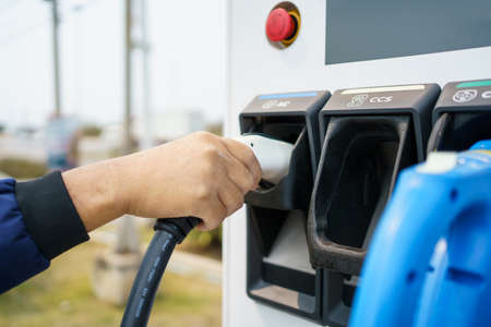 Asian man preparing to charge his electric car or EV at charging station, man holding a Type 2 BEV charging connector. Electric Vehicle or EV car and zero emission concept.の写真素材