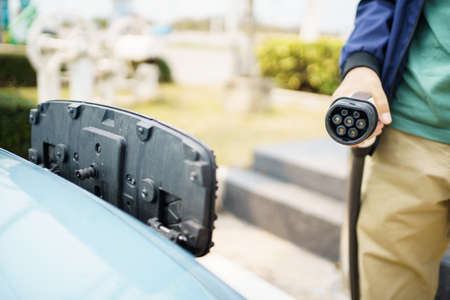 Asian man preparing to charge his electric car or EV at charging station, man holding a Type 2 BEV...