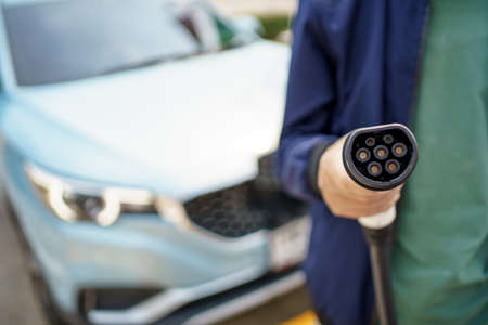 Asian man preparing to charge his electric car or EV at charging station, man holding a Type 2 BEV charging connector. Electric Vehicle or EV car and zero emission concept.の写真素材