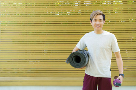 Active Asian sportsman preparing - unrolling an exercise or Yoga mat, healthy and fit body of Asian sport man preparing a workout yoga mat for body weight and cardio exercise.の写真素材