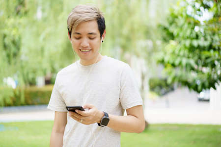 Handsome Asian young sportsman posing and smiling to the camera while his running exercise, man listening a music on smartphone while practicing running workout. Happy Asian athlete smiling.の写真素材
