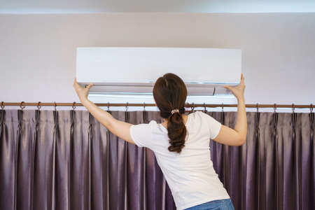 Asian woman cleaning a dirty and dusty air conditioning filter in her house. Housewife removing a dusty air conditioner filter.の写真素材