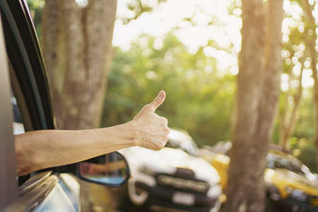 Unrecognizable Asian woman driver showing a thumb up outside the vehicle while driving a car. Happy woman driver or passenger showing her thumb up during in the car. Safety trip and freedom concept.の写真素材