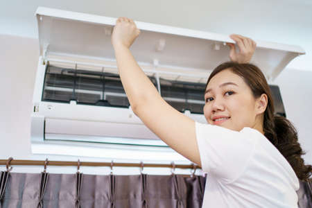 Asian woman cleaning a dirty and dusty air conditioning filter in her house. Housewife removing a dusty air conditioner filter.の写真素材