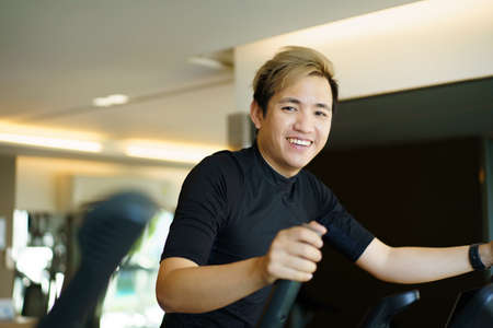 Active Asian young man making a cardio exercise on the elliptical exercise machine in the gym. Fat burn and body muscle building. bodybuilding workout concept.の写真素材