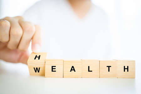 Words Health and Wealth on the wooden block close up, man turning the words between health and wealth. The conceptual of healthcare - wellbeing and security in financial.の写真素材