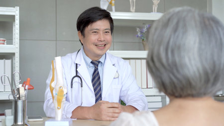Asian young woman taking her mother to see an orthopedic doctor at hospital. Elder woman talking and having a consulting with orthopedic doctor about disease. Wellness and health care concept.の写真素材