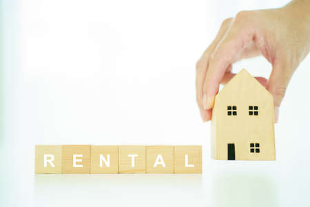 Wooden blocks with the word "rent" and basic wooden house model. Housing - real estate rental and investment concept.の写真素材