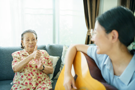 Asian elder woman playing an acoustic guitar and let her granddaughter taking a video on smartphone close up with copyspace. Elder Asian woman making a online video live streaming on social network.の写真素材