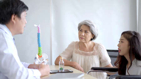 Asian young woman and her mother taking to doctor at hospital about orthopedic disease. Woman having the office syndrome illness and comes to see the specialist doctor.の写真素材