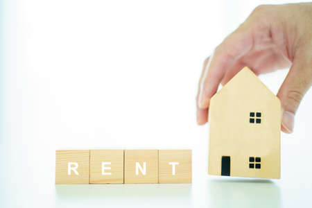 Wooden blocks with the word "rent" and basic wooden house model. Housing - real estate rental and investment concept.の写真素材