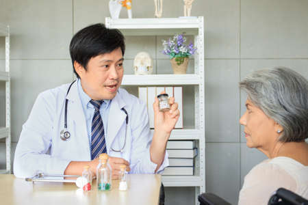 Asian elder woman talking to doctor in the doctor office in hospital about medicine usage and treatment. Asian doctor giving an advice and explaining to elder female patient.の写真素材