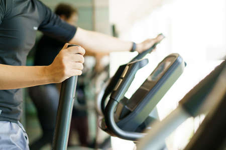 Active Asian young man making a cardio exercise on the elliptical exercise machine in the gym. Fat burn and body muscle building. bodybuilding workout concept.の写真素材