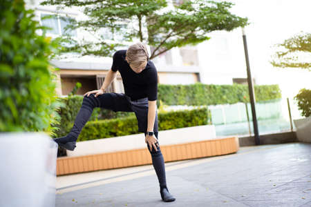 Happy Asian young sportsman doing a lower and upper body stretching before making an exercise in a park, stretching and workout concept. Sport man making a cardio and weight training workout.の写真素材