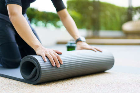 Active Asian sportsman unroll an exercise mat on the floor, healthy and fit body of Asian sport man preparing a workout yoga mat for body weight and cardio exercise.の写真素材