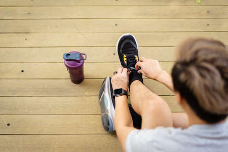 Happy Asian young sportsman trying to tie shoelaces before getting an exercise, man preparing for out workout. Healthy Asian young sporty man tie up a running shoes before running.の写真素材