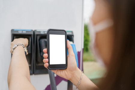 Empty screen of mockup smartphone isolated with clipping path. Asian young woman using ev charging application on smartphone connect with the charging station, BEV or electric vehicle charging stationの写真素材