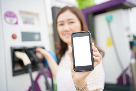 Empty screen of mockup smartphone isolated with clipping path. Asian young woman using ev charging application on smartphone connect with the charging station, BEV or electric vehicle charging stationの写真素材