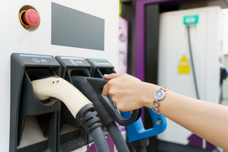 Unrecognizable Asian woman holding a DC - CCS type 2 EV charging connector at EV charging station, woman preparing an EV - electric vehicle charging connector for recharge a vehicle.の写真素材