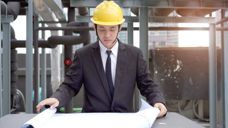 Professional Asian cilvil engineer reviewing and inspecting the building blue print at the construction site. Asian foreman working at the construction site on the building rooftop.の写真素材